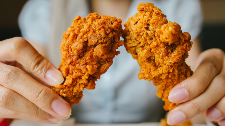 Hands holding fried chicken.