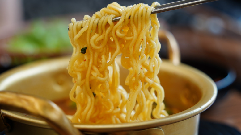 Chopsticks holding cooked instant ramen from a bowl