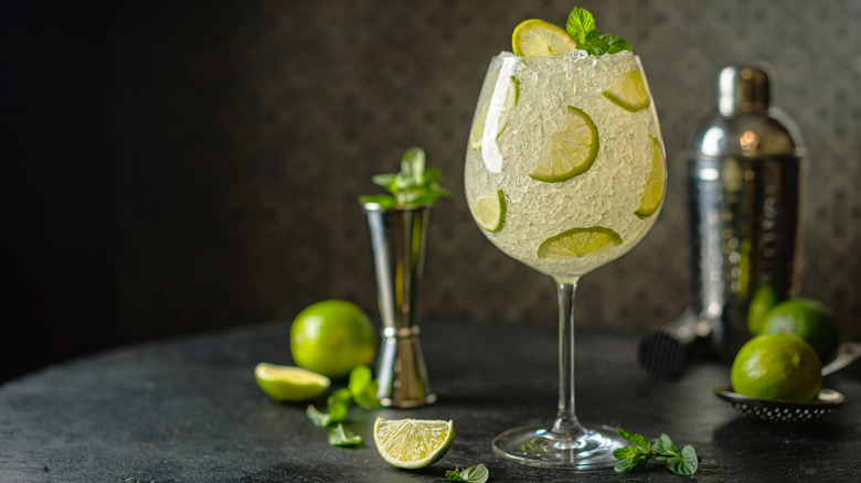 a margarita with limes and a metal cocktail shaker