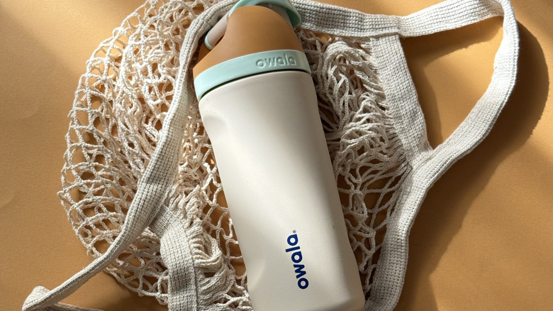 A tan and beige Owala reusable water bottle laying on a mesh shopping bag