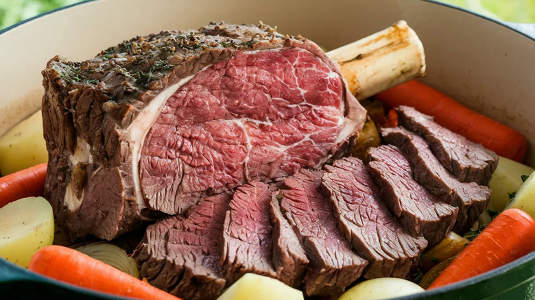 Bone-in prime rib roast in a pot with onions, potatoes, and carrots