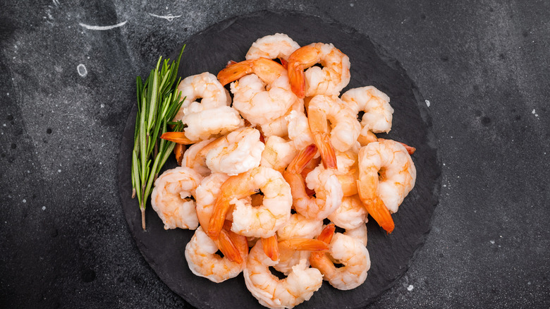 A pile of pink shrimp is arranged on a black plate.