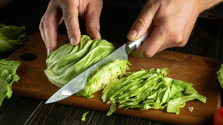 A hand chopping cabbage with a knife.