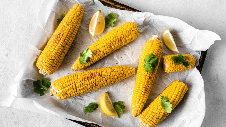 A tray of roasted corn with cilantro and lemon wedges