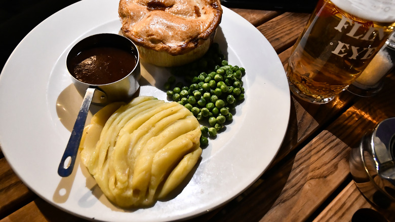 Creamy mashed potatoes on a plate with a peas, gravy, and a Yorkshire pudding