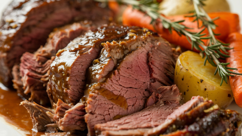 A closeup of a sliced pot roast with vegetables, rosemary, and gravy