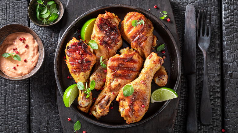 Grilled chicken legs served on a black plate with limes.