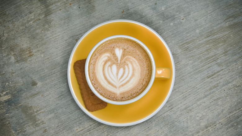A latte on a yellow plate with cookie