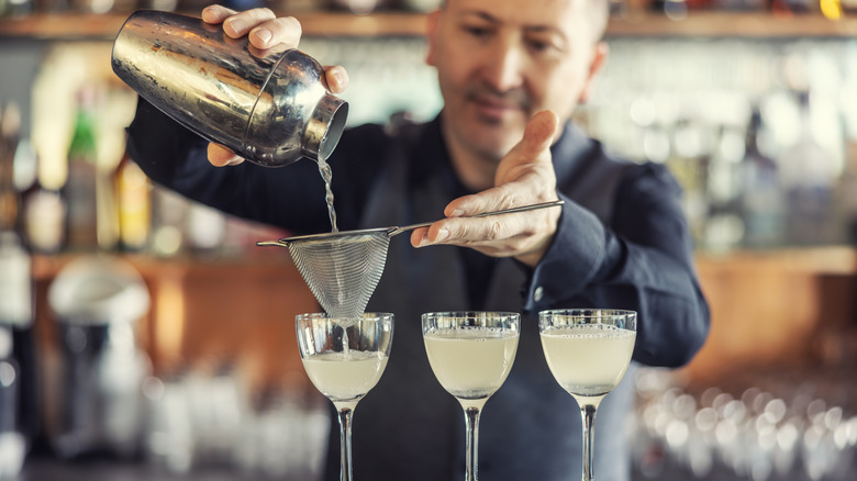 A bartender pours three cocktails from a cocktail shaker.