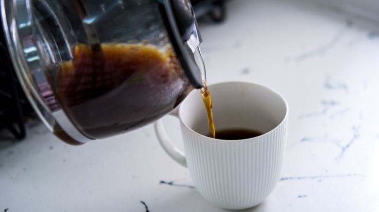 Coffee from a glass pot being poured into a white mug sitting on a kitchen counter.