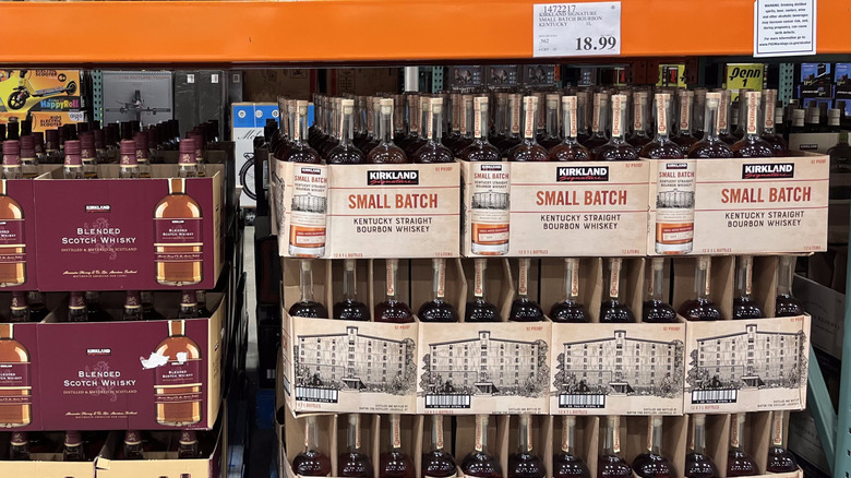 Many cases of Kirkland Signature Small Batch Kentucky Straight Bourbon Whiskey, each holding several bottles, sit stacked on Costco shelves.