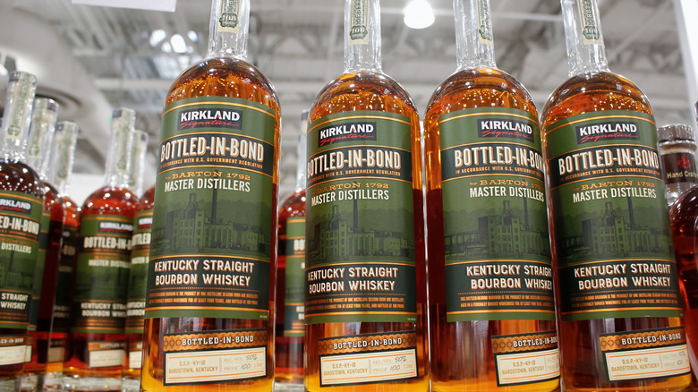 Numerous bottles of Kirkland Signature's Bottled-in-Bond Kentucky Straight Bourbon Whiskey sit on shelves in a Costco warehouse store.