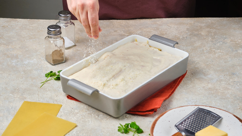 Chef sprinkling cheese on unbaked lasagna