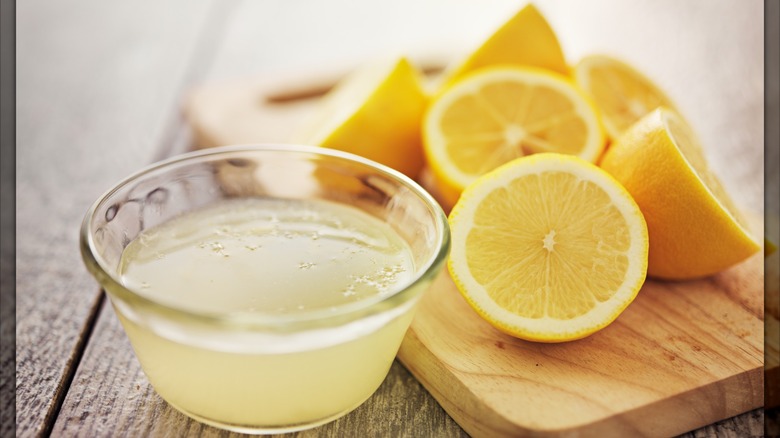Glass bowl of lemon juice with halved lemons