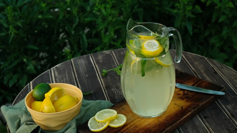 Pitcher of lemonade on outdoor table next to bowl of lemons