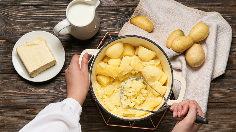 Hand mashing potatoes in a large pot. 