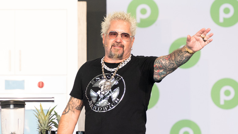 Guy Fieri waving out to a crowd while speaking at an event