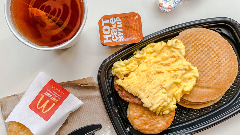 A plate of scrambled eggs with hot cakes plate at McDonald's next to a drink and hash browns