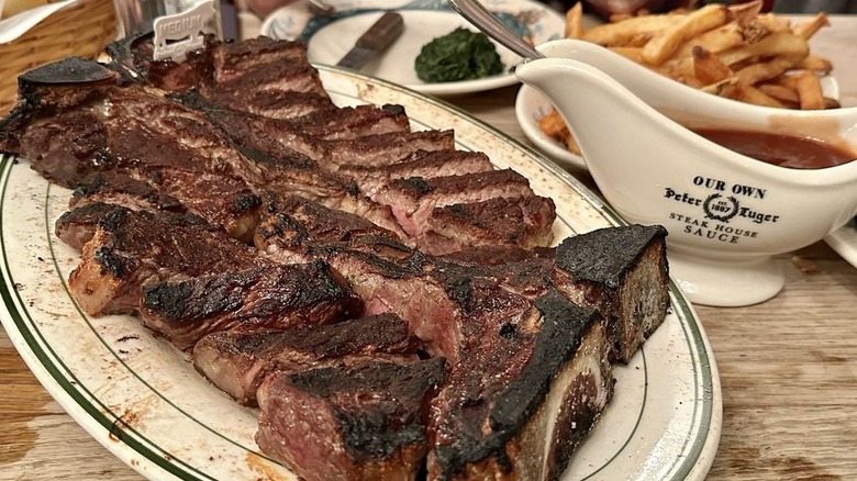 A sliced bone-in steak for three with steak sauce, french fries, and creamed spinach from Peter Luger Steakhouse in New York City