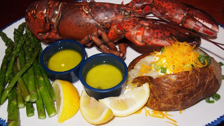 A steamed lobster from Red Lobster with baked potato, asparagus, drawn butter, and lemons, served on a white plate