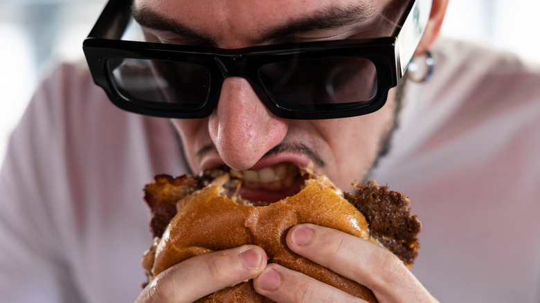 A man in sunglasses biting into a beef burger.