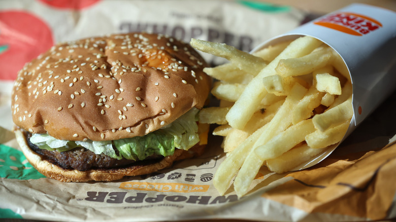 A Whopper sitting on its wrapper next to fries in a carton with Burger King logo