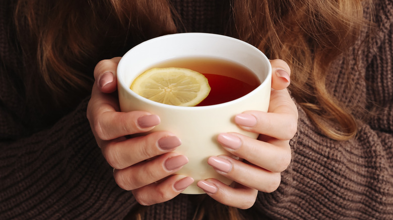 Female hands holding a mug of lemon tea