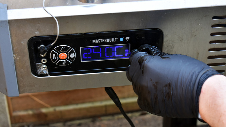 Hands adjusting temperature on smoker