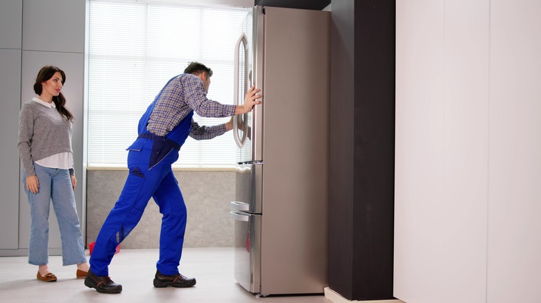 Male installing a new fridge for his female neighbor