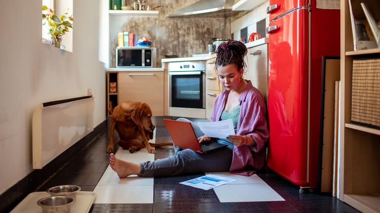 Young woman sitting on the kitchen floor calculating the cost of installing a new fridge