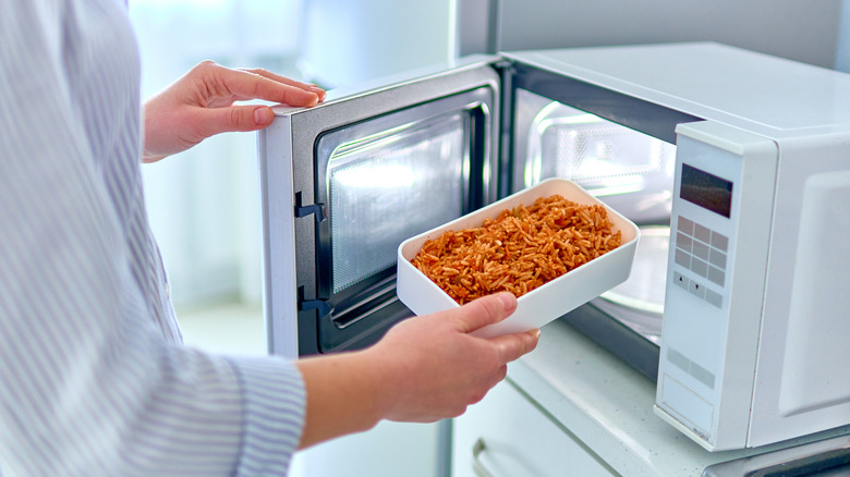 Hand putting a container of rice into the microwave.