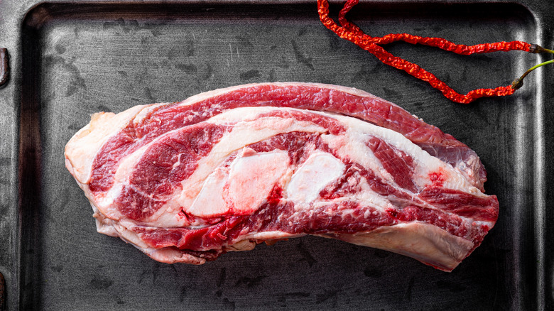 A fresh, raw beef brisket on a metal pan, chiles above, with lots of fat on the exterior.