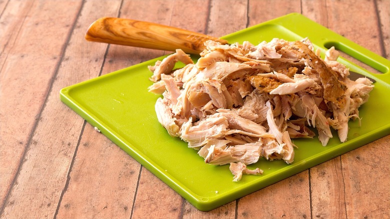 Pulled rotisserie chicken on green cutting board