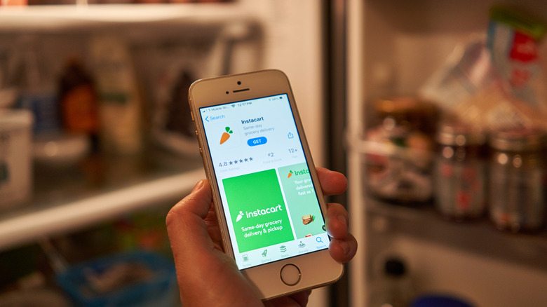 A person's hand holding a cellphone with the Instacart app page open on the App Store
