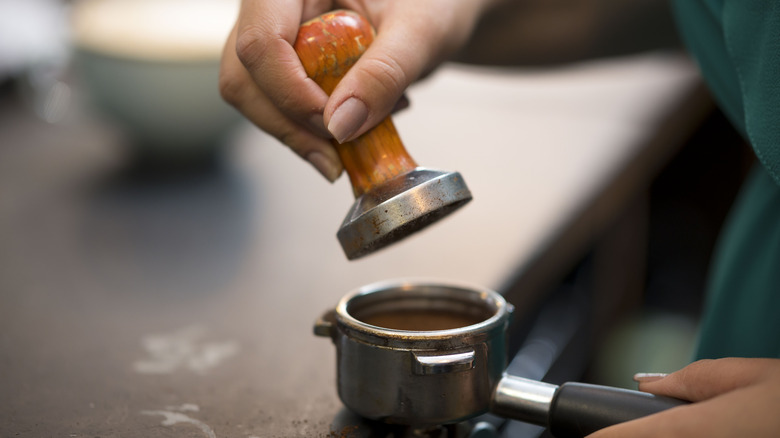 A woman using a tamper in a coffee shop.