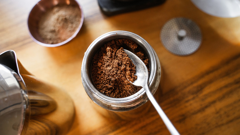 Spooning ground coffee into a moka pot.
