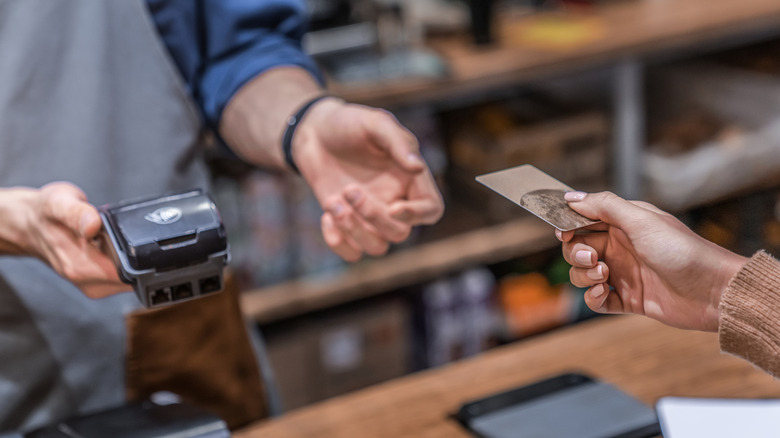 One person's hand is seen giving a credit card for payment to another person wearing an apron.