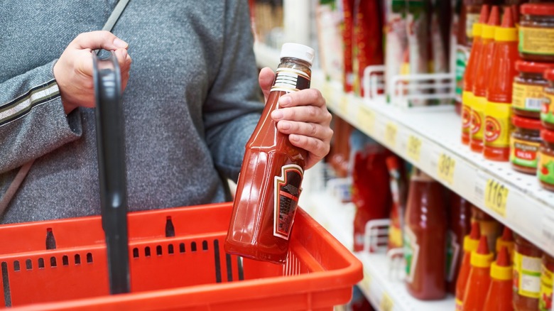 Shopper putting ketchup bottle in a red hand basket
