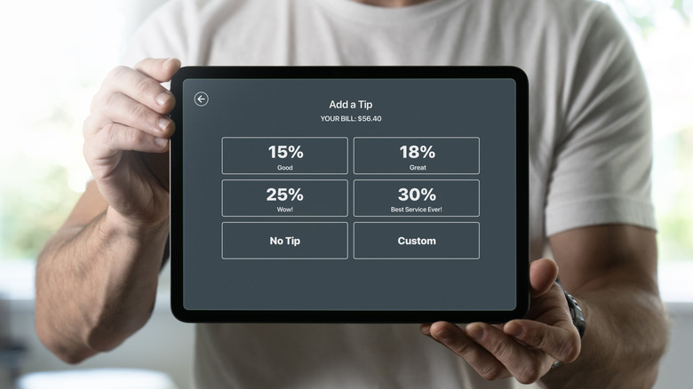 A person in a white shirt holds up a tipping percentage screen on a tablet
