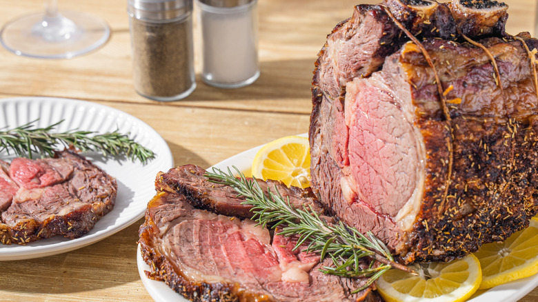 Cooked prime rib roast on serving tray with a sprig of rosemary