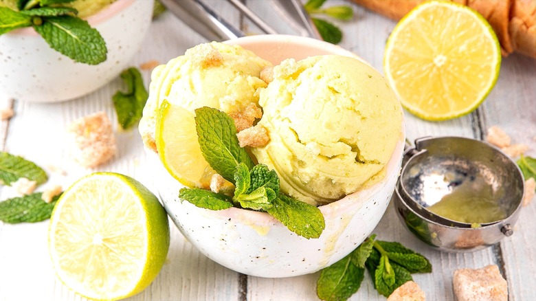 A few scoops of lime ice cream with vanilla cookie crumbles and fresh mint leaves in a small, white, speckled bowl