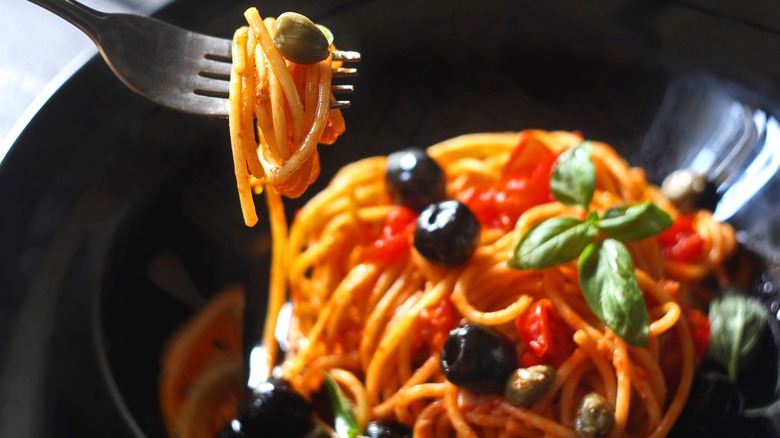 closeup of a fork picking up spaghetti with capers and black olives