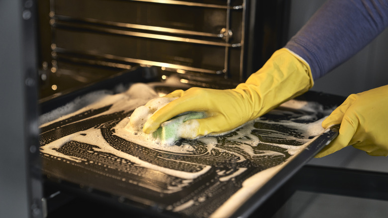 Person wearing yellow gloves scrubbing a pull-out oven tray