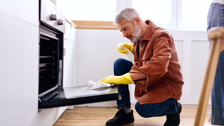 Man wearing yellow gloves wiping down the inside of an oven door