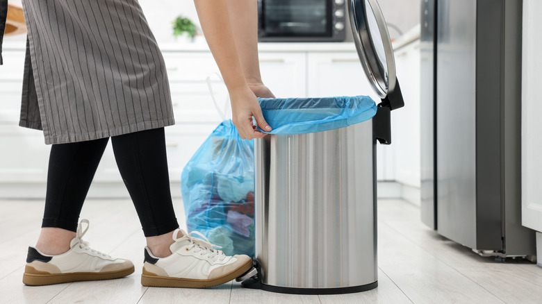 A person changes the bag in a kitchen trash can