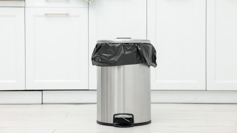 A stainless steel trash can sits in front of white cupboards