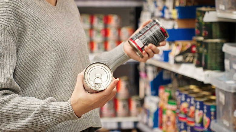 Person holding a can of food in each hand at the grocery store