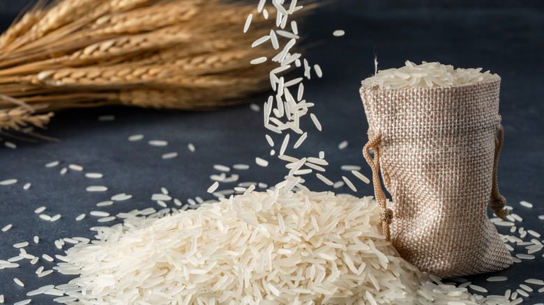 Grains of white rice falling onto a slate surface with a bag of rice and whole rice nearby.