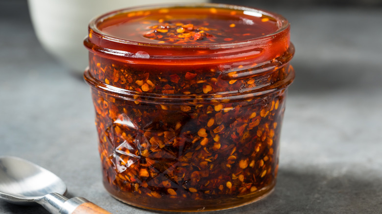 A clear glass jar of chili crisp in close-up.