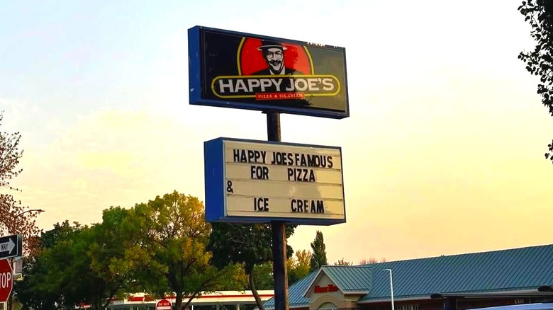 A big sign of Happy Joe's outdoors with a text that reads at the bottom that reads, "Happy Joe's famous for pizza & ice cream."